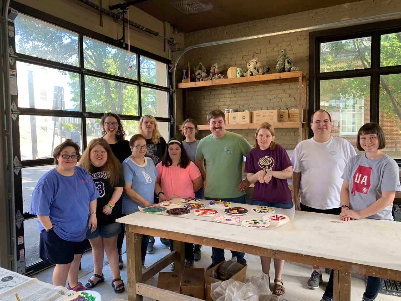 a group of adults with and without disabilities standing behind a table with art supplies posing for a photo