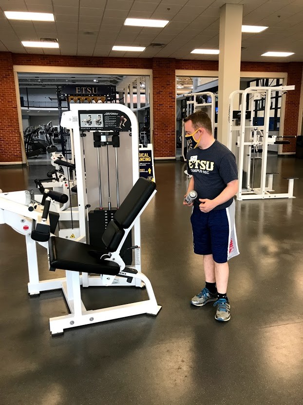 Garrison Buchanan, Access ETSU student Garrison Buchanan cleans the fitness equipment. A Young white man with Down syndrome dressed in athletic gear wipes down fitness equipment in a gym.
