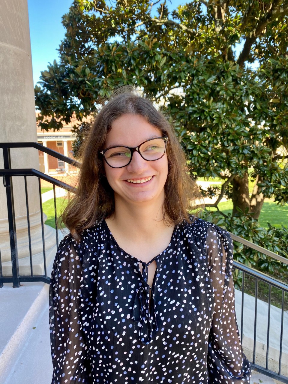 Lauren Ciangfaglione Lauren, a young white woman with glasses and a visual difference, short dark blonde hair and a flowered blouse outdoors at Lipscomb, smiling