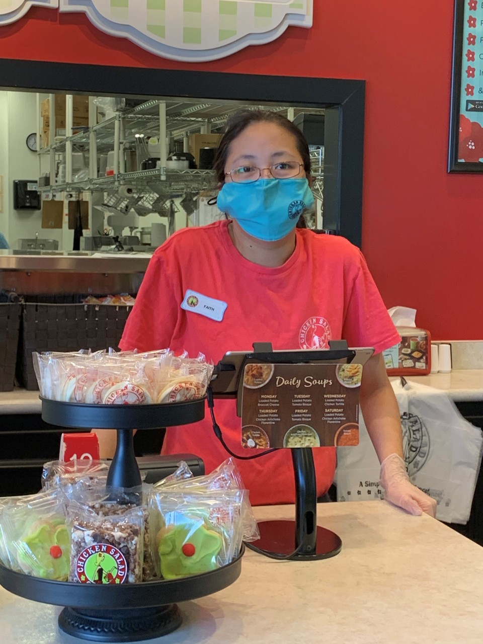 Faith Moore, Union EDGE Union student Faith wearing a bright pink shirt and standing behind the front counter at the restaurant where she works, in front of the cash register. She’s wearing a mask and a name tag.
