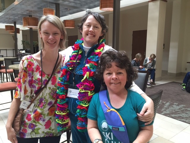 Three young, white women pose in a hotel lobby with their arms around each other, smiling broadly