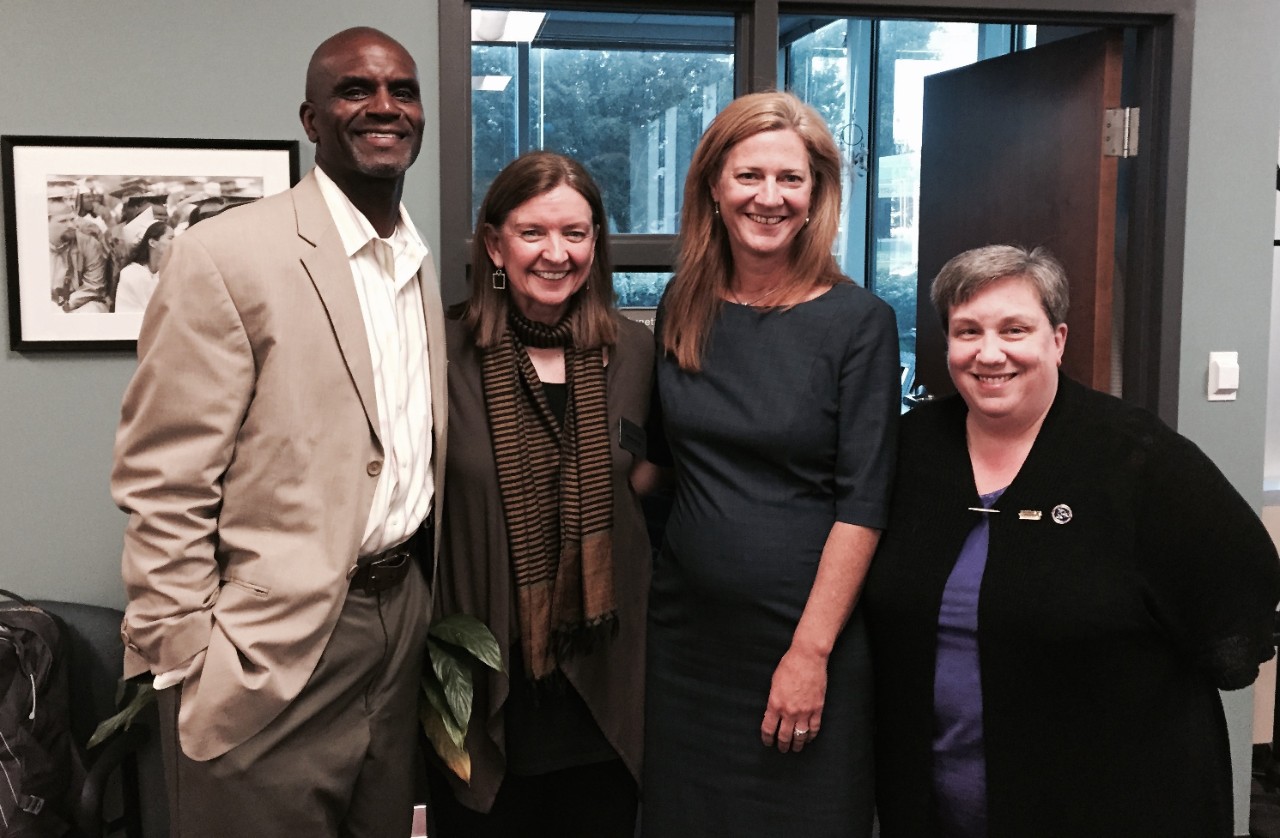 Wanda stands between a Black man in a white shirt, light suit jacket and dress pants on the left and white woman who is wearing a dark dress with ¾ sleeves and has long, straight, light colored hair. Alicia Cone is on the far right – a white woman with short, light hair and wearing a black sweater over a blue top