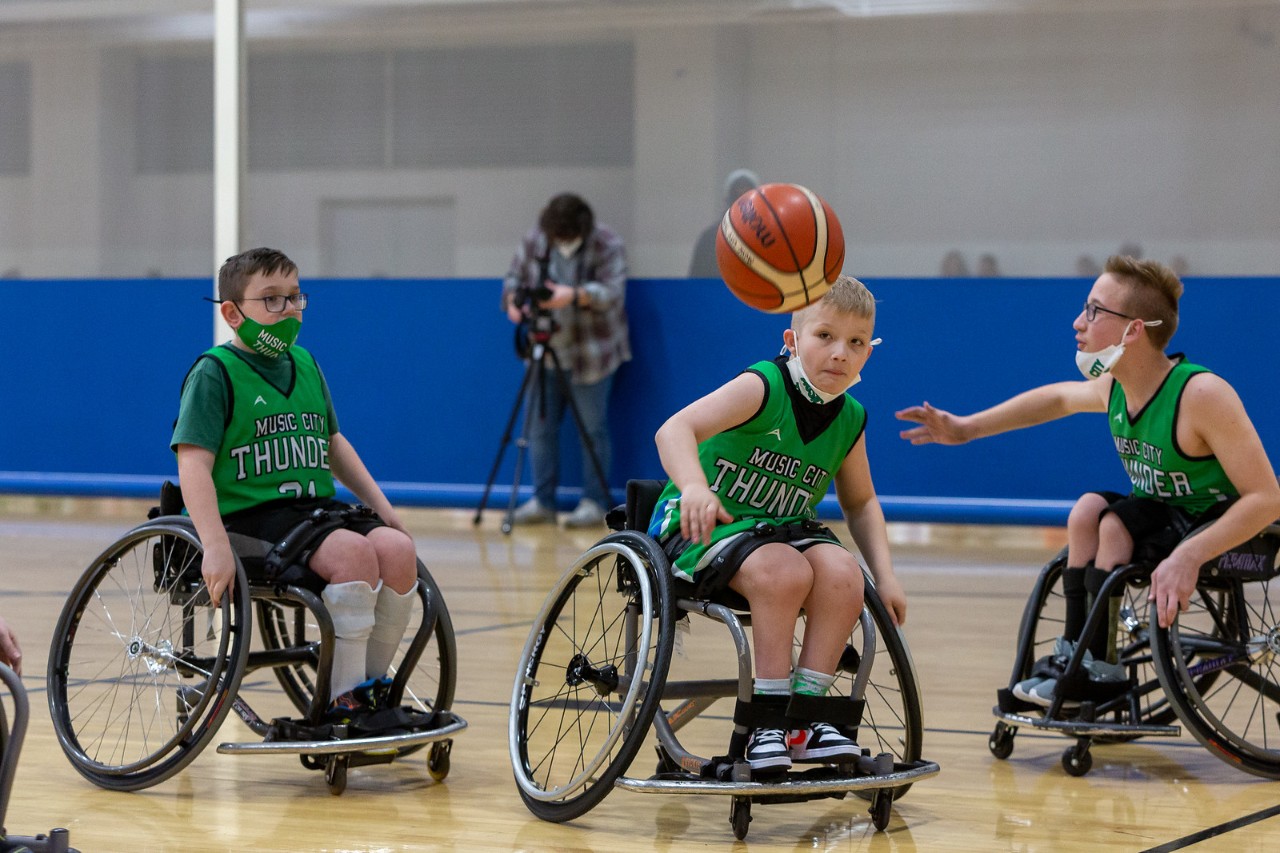 Music City Thunder youth wheelchair basketball team 3 young boys in green sports jerseys and seated in wheelchairs play basketball in a gym