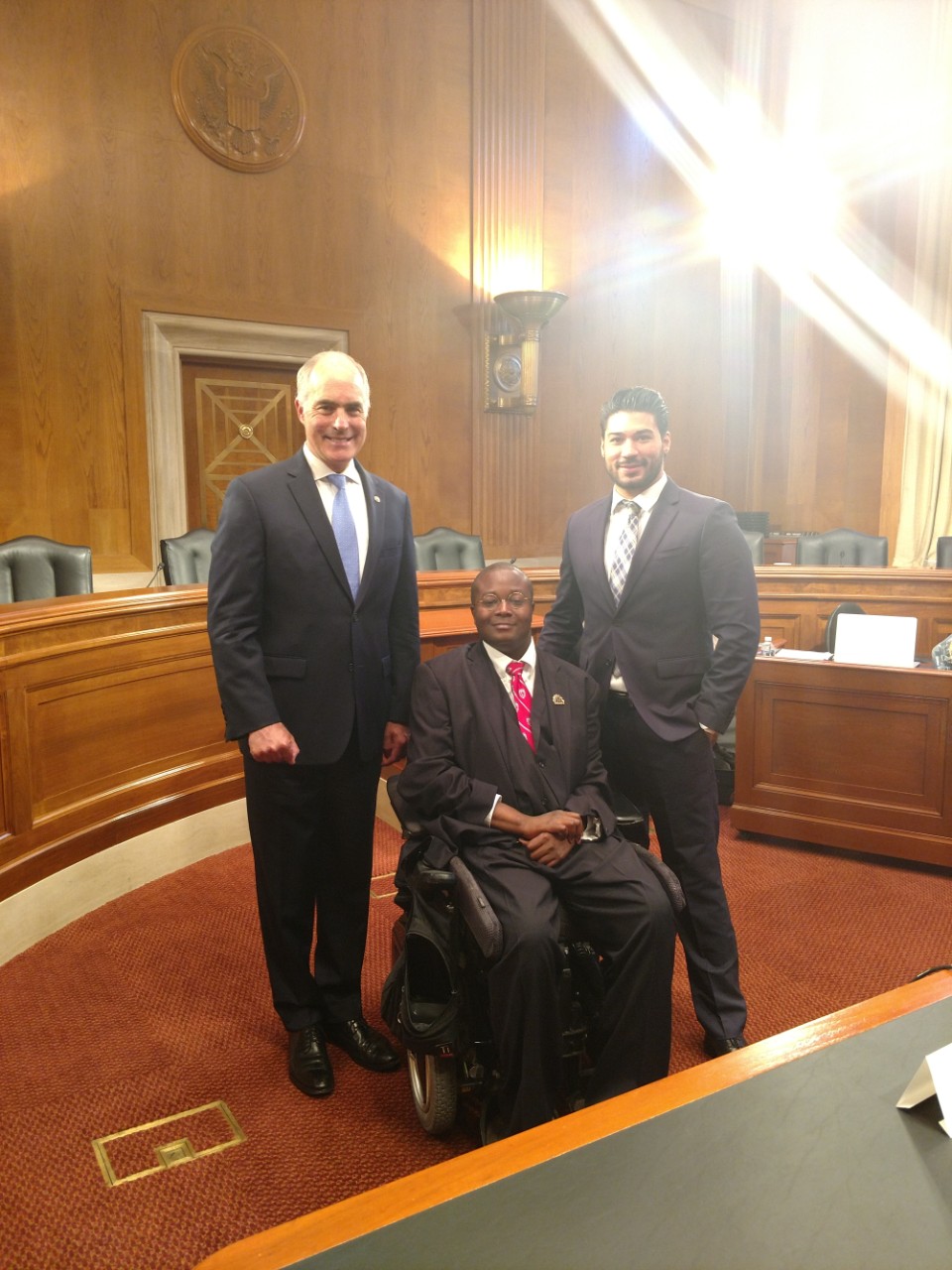 BG94 Edward Mitchell testifies 2 There are three men posing in a federal government meeting room in Washington, DC. They are Senator Bob Casey, Christopher J. Rodriguez, Director of Public Policy, and Edward Mitchell, the subject of the article. All three men are wearing suits and ties, and Edward Mitchell is sitting in a power wheelchair.