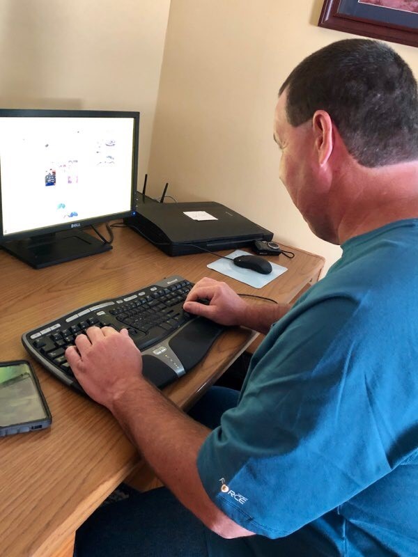 BG99 Jeff at computer, STAR Center article a middle-aged man, Jeff, sitting at a computer, typing on a keyboard. The caption reads: “Jeff uses accessibility software and voice technology to conduct business on his laptop.”