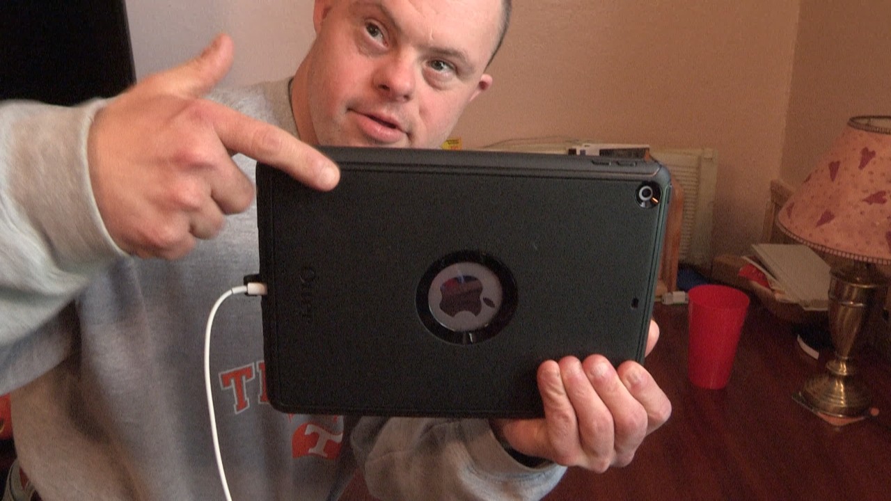 96 Brad and Tech 4 Brad is pointing to a black iPad that has a white power cord attached to it