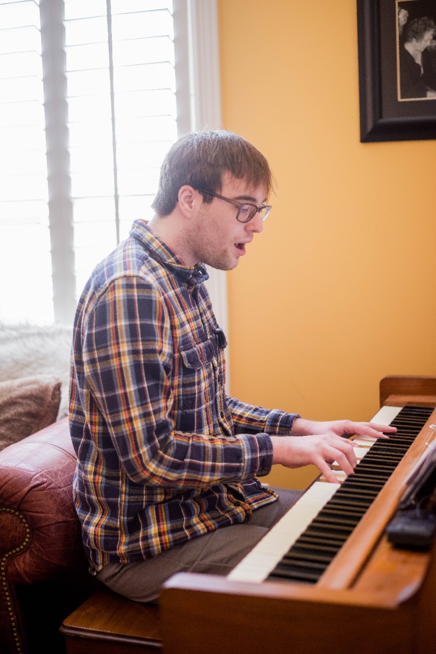 Ben, a 21yo man, sits at an antique piano singing and playing the keys